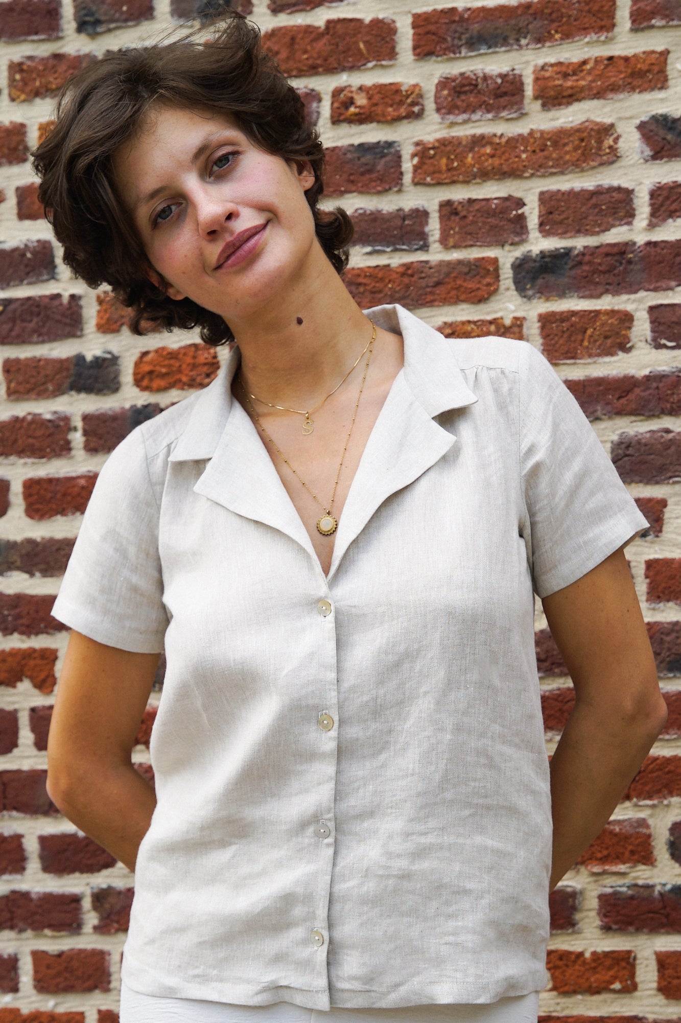 Femme portant une chemise en lin gris clair, avec un col tailleur minimaliste, des manches courtes ainsi que des boutons en nacre pour refermer sur le devant.