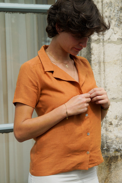 Femme portant une chemise en lin orange, avec un col tailleur et des manches courtes. La chemise se ferme par des boutons en nacre sur le devant.
