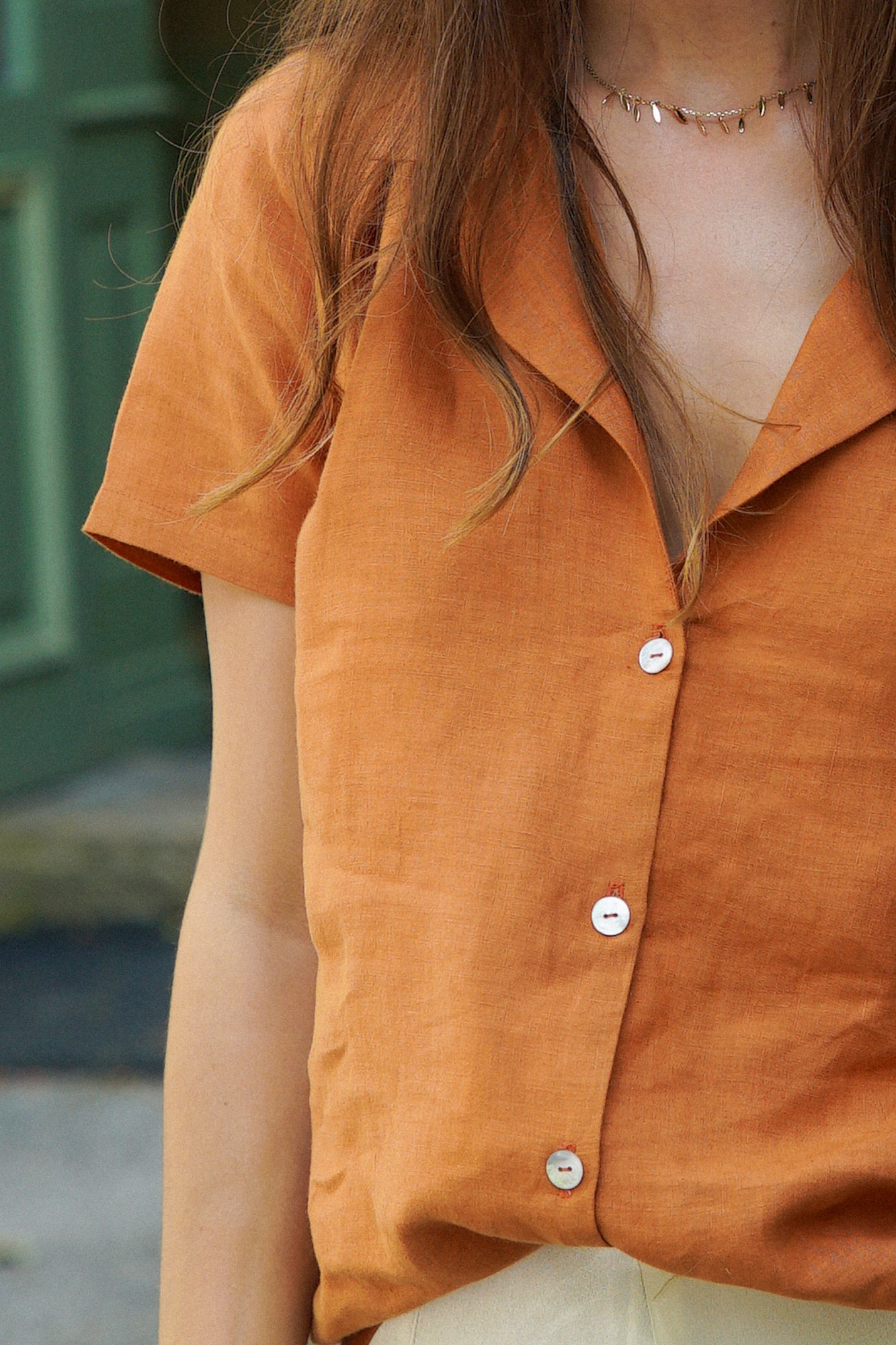 Femme portant une chemise en lin orange, avec un col tailleur et des manches courtes. La chemise se ferme par des boutons en nacre sur le devant.