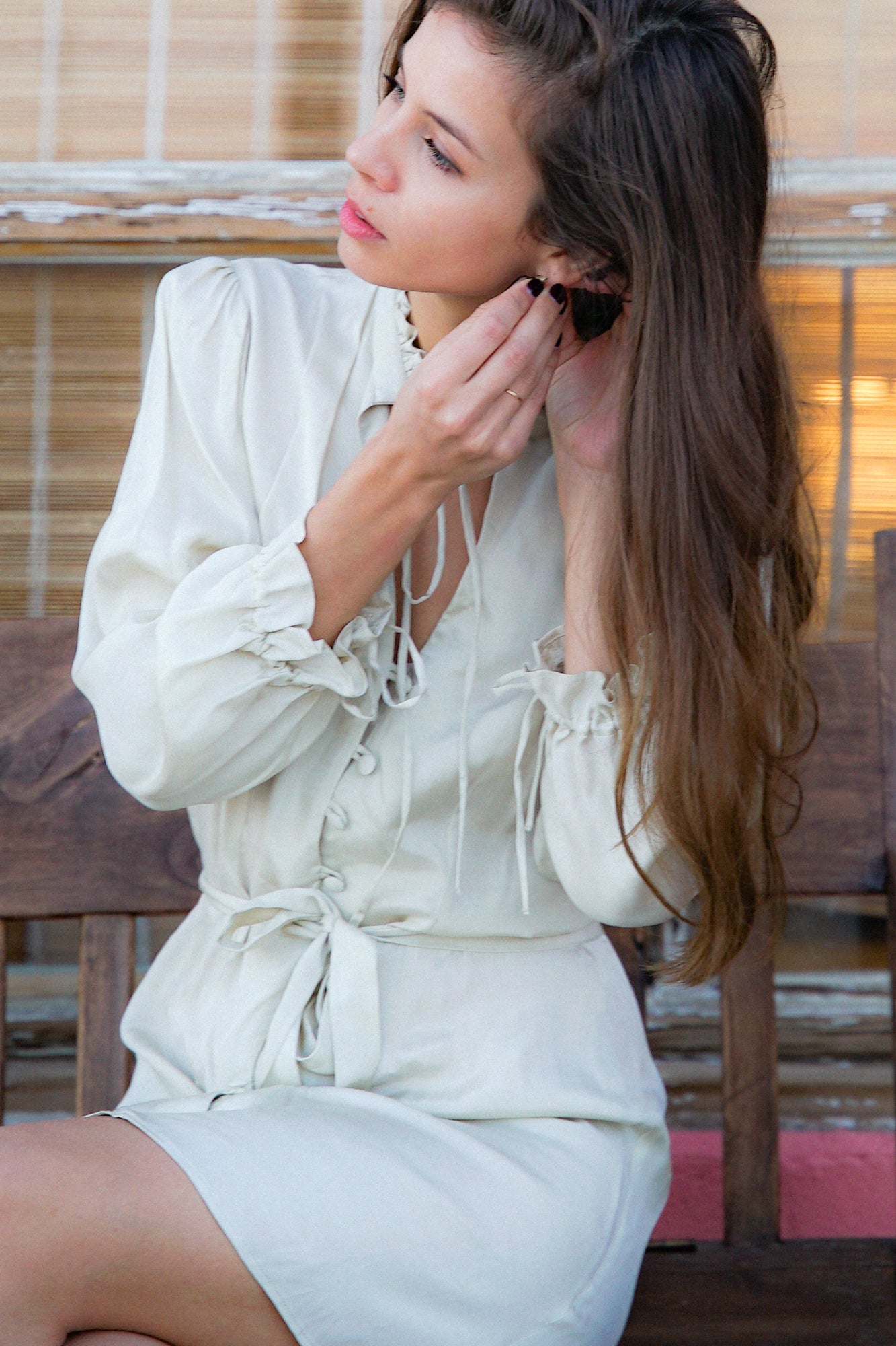Femme portant une robe blanc cassé avec un col froufrou montant qui se resserre par des brides au niveau du cou.
